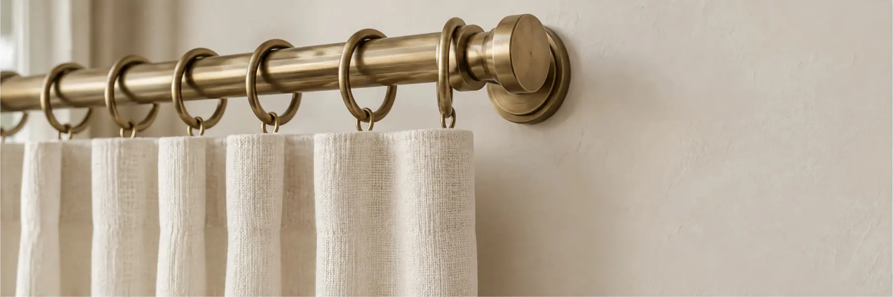 Brushed brass curtain rod and rings holding an ivory woven curtain